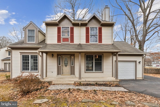 traditional-style home featuring a porch, a chimney, an attached garage, and aphalt driveway