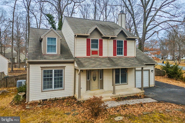 traditional-style house featuring a garage, central AC unit, a chimney, aphalt driveway, and covered porch