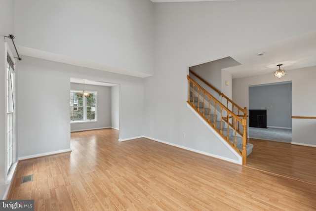 unfurnished living room featuring light wood-style floors, visible vents, stairway, and baseboards