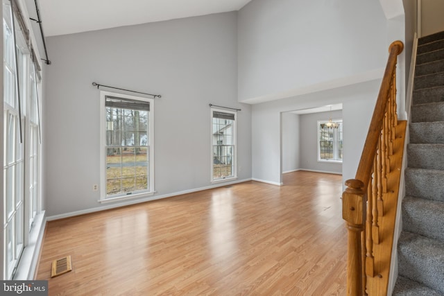 unfurnished living room featuring light wood-style flooring, stairway, plenty of natural light, and visible vents