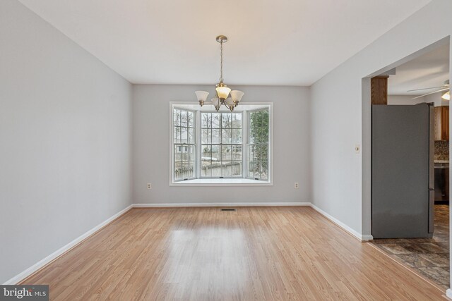 unfurnished dining area with ceiling fan with notable chandelier, visible vents, baseboards, and wood finished floors