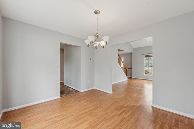 empty room featuring stairs, light wood-type flooring, baseboards, and an inviting chandelier