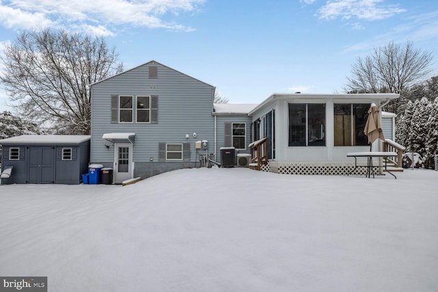 snow covered property featuring a storage unit, a sunroom, and central air condition unit