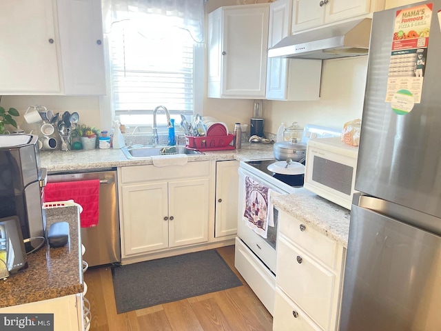 kitchen with appliances with stainless steel finishes, white cabinetry, sink, light stone countertops, and light wood-type flooring