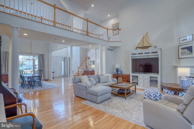 living room featuring ornate columns, a towering ceiling, an inviting chandelier, and light wood-type flooring