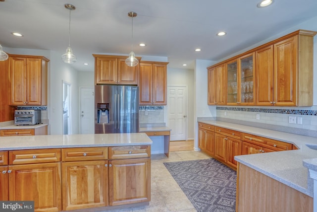 kitchen with light tile patterned flooring, pendant lighting, backsplash, light stone counters, and stainless steel refrigerator with ice dispenser