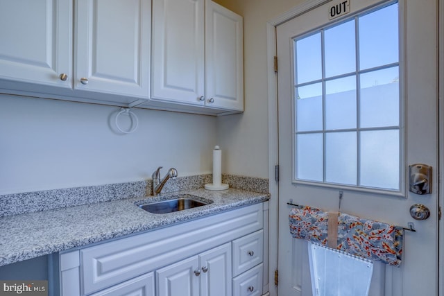 kitchen with light stone countertops, sink, and white cabinets