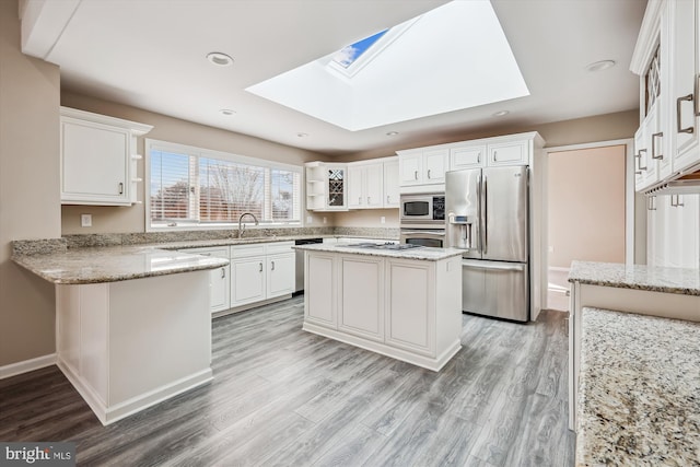 kitchen featuring white cabinetry, a skylight, stainless steel appliances, light stone countertops, and a kitchen island