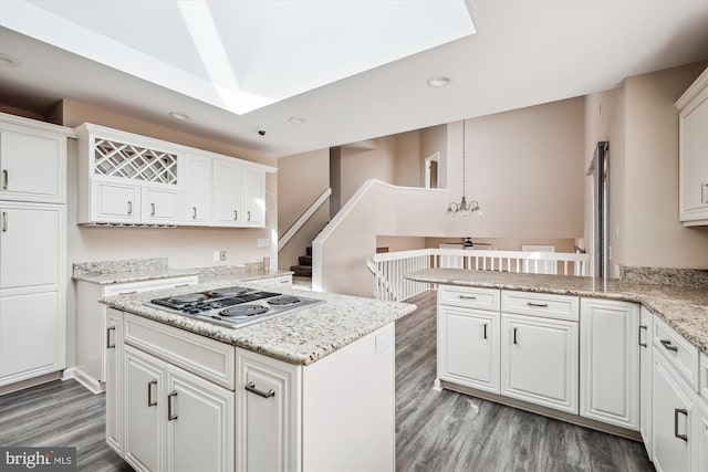 kitchen featuring white cabinetry, wood-type flooring, stainless steel gas cooktop, light stone counters, and kitchen peninsula