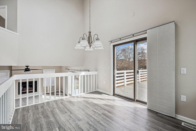 unfurnished dining area featuring hardwood / wood-style flooring, ceiling fan with notable chandelier, and a high ceiling