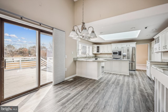 kitchen with pendant lighting, a skylight, white cabinetry, stainless steel appliances, and light hardwood / wood-style flooring