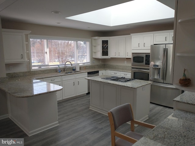 kitchen with appliances with stainless steel finishes, light stone countertops, a kitchen island, and white cabinets