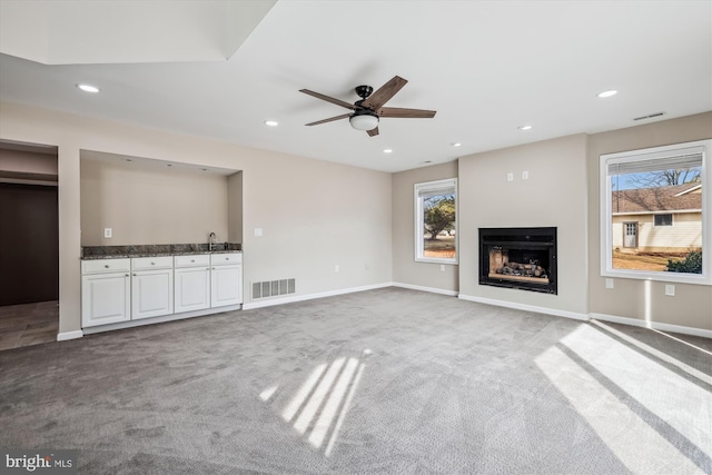 unfurnished living room with sink, ceiling fan, and carpet flooring