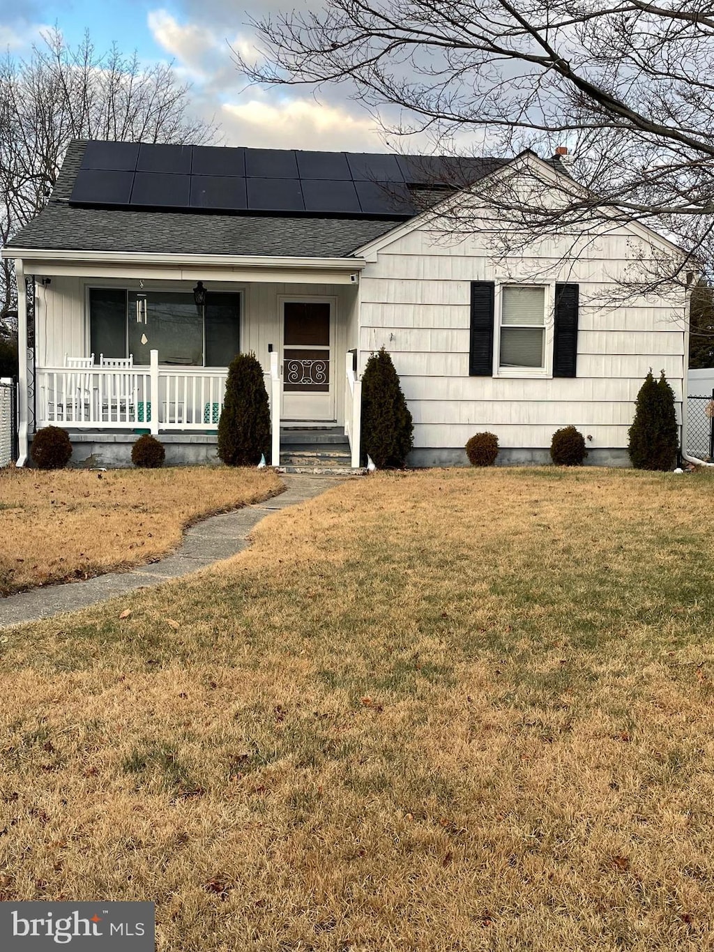 view of front facade featuring a front lawn, solar panels, and a porch