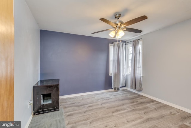 unfurnished living room featuring light hardwood / wood-style floors, ceiling fan, and a wood stove