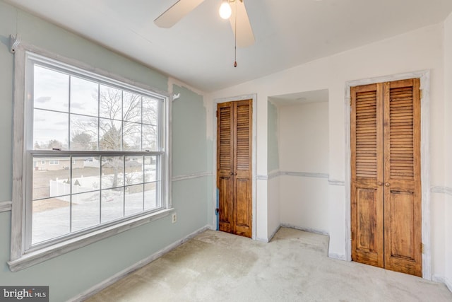 unfurnished bedroom featuring multiple closets, light colored carpet, vaulted ceiling, and multiple windows