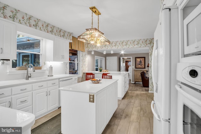 kitchen featuring sink, hanging light fixtures, a kitchen island, white appliances, and white cabinets