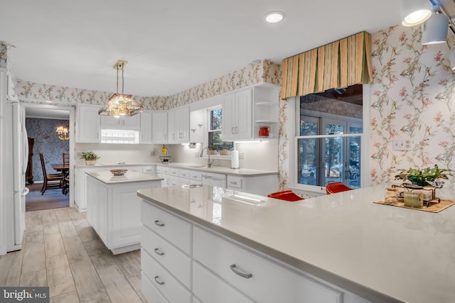 kitchen featuring hanging light fixtures, light wood-type flooring, a kitchen island, white appliances, and white cabinets