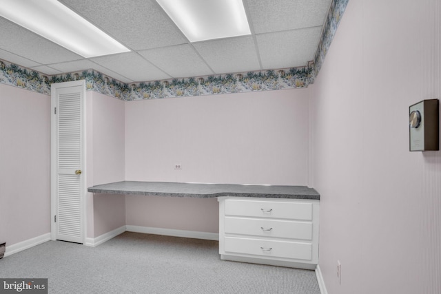 unfurnished office with a drop ceiling, built in desk, and light colored carpet