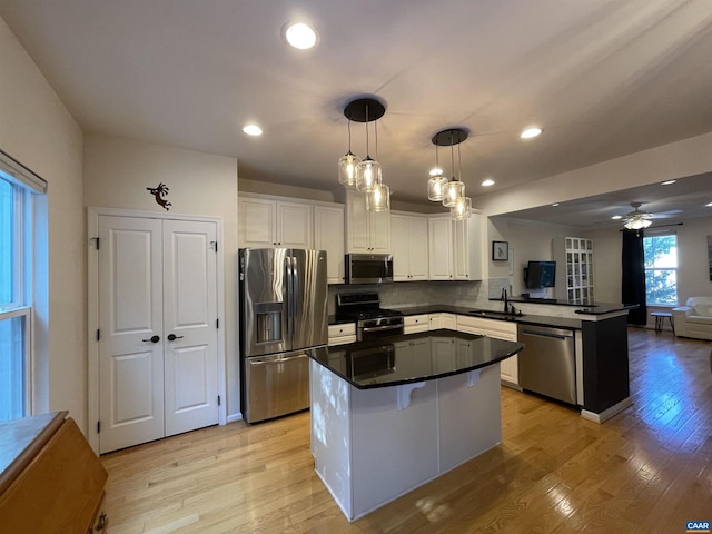 kitchen featuring pendant lighting, sink, white cabinetry, stainless steel appliances, and kitchen peninsula