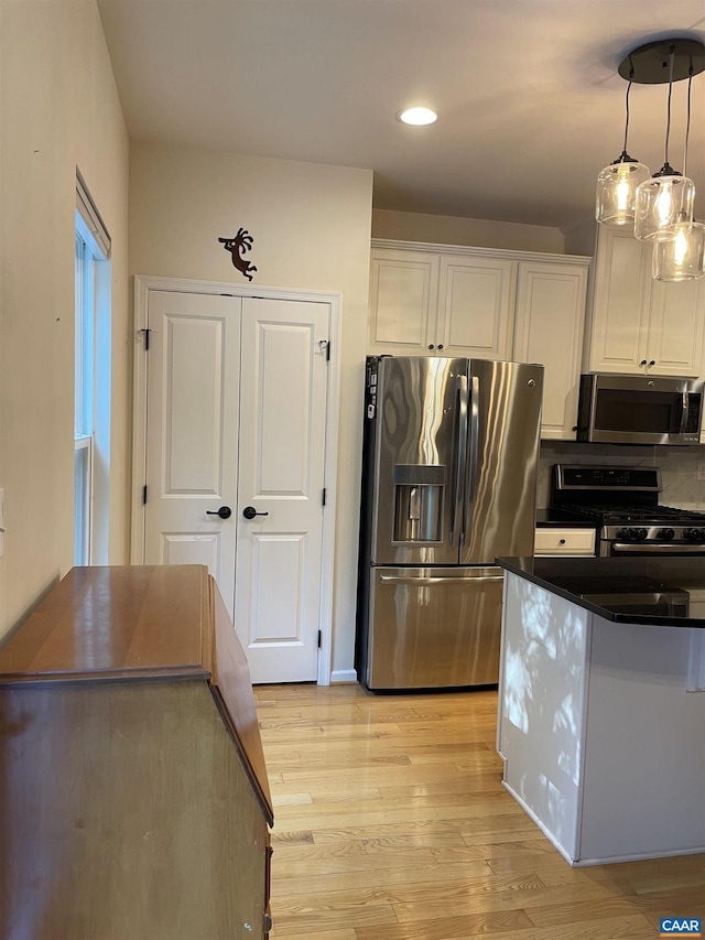 kitchen with white cabinetry, hanging light fixtures, stainless steel appliances, and light hardwood / wood-style floors