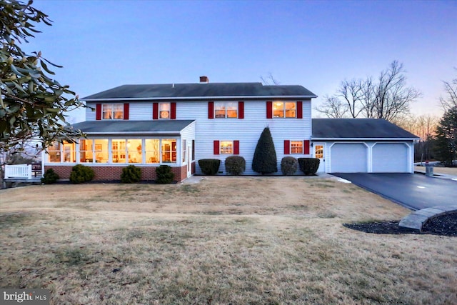 view of front of home with a garage, a sunroom, and a lawn