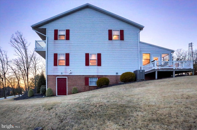 back house at dusk featuring a wooden deck, a yard, and central AC