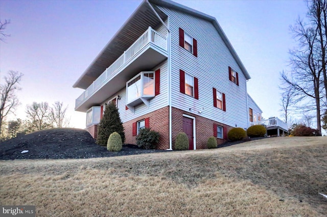 property exterior at dusk with a balcony and a lawn