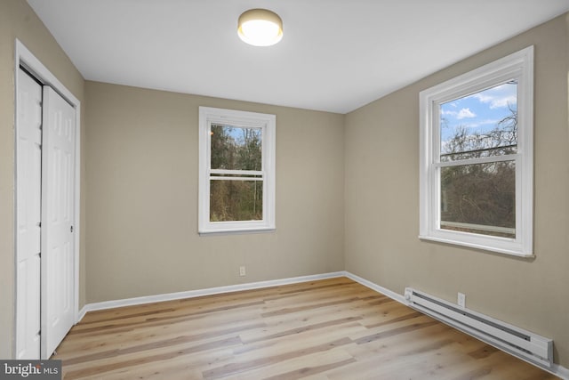 unfurnished bedroom featuring light wood-type flooring, baseboard heating, and a closet