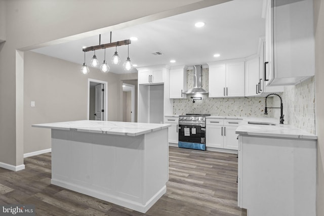 kitchen featuring wall chimney range hood, sink, white cabinetry, light stone counters, and stainless steel range oven