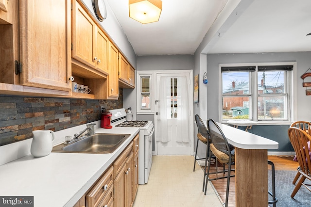 kitchen with a breakfast bar area, sink, white range with gas stovetop, and backsplash