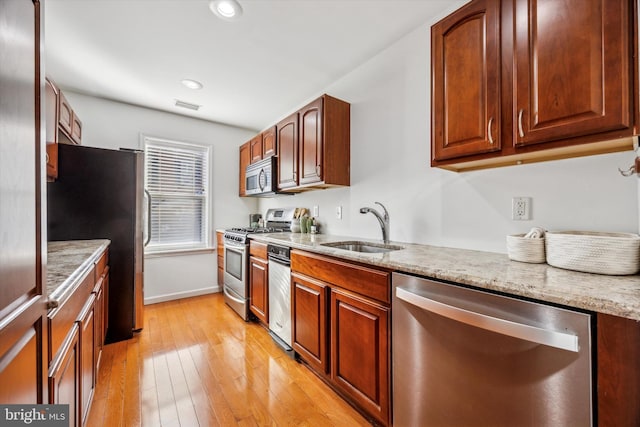 kitchen featuring light stone counters, appliances with stainless steel finishes, light hardwood / wood-style floors, and sink