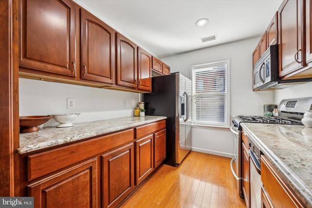 kitchen with stainless steel appliances, light stone countertops, and light wood-type flooring