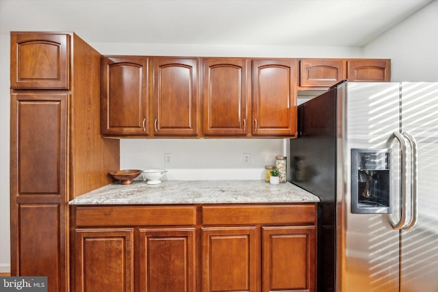 kitchen featuring light stone counters and stainless steel refrigerator with ice dispenser