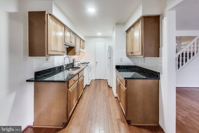 kitchen with sink, dark stone countertops, white appliances, and light hardwood / wood-style floors