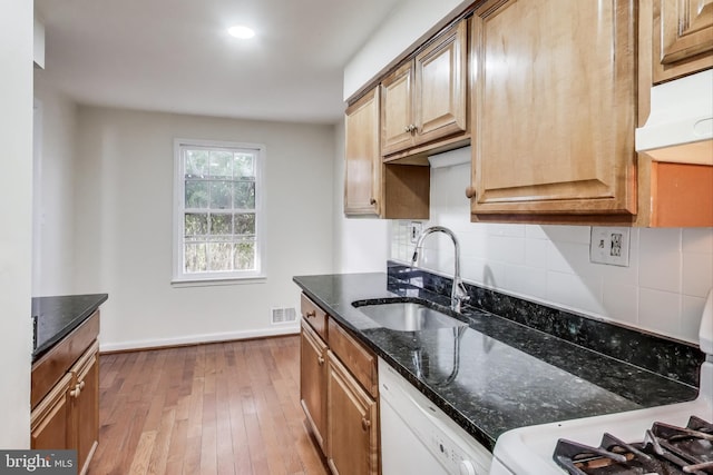 kitchen with sink, tasteful backsplash, dishwasher, dark stone counters, and light hardwood / wood-style floors