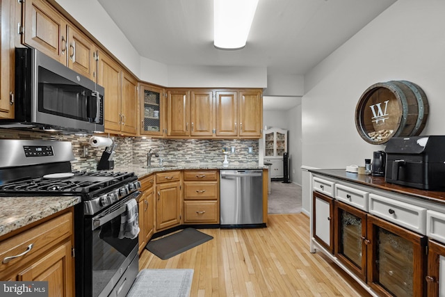 kitchen with sink, appliances with stainless steel finishes, light stone countertops, light hardwood / wood-style floors, and decorative backsplash