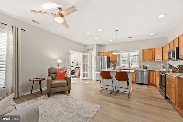 kitchen featuring a kitchen bar, light stone counters, appliances with stainless steel finishes, a kitchen island, and pendant lighting