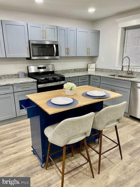 kitchen with gray cabinets, appliances with stainless steel finishes, sink, light stone counters, and light hardwood / wood-style floors