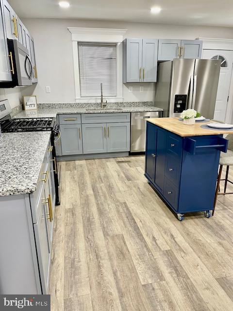 kitchen with appliances with stainless steel finishes, sink, light stone counters, and light hardwood / wood-style flooring