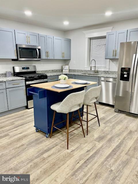 kitchen with sink, light hardwood / wood-style flooring, appliances with stainless steel finishes, a kitchen island, and a kitchen bar