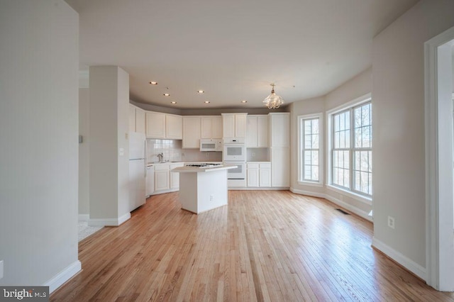 kitchen featuring hanging light fixtures, white cabinetry, a kitchen island, and white appliances