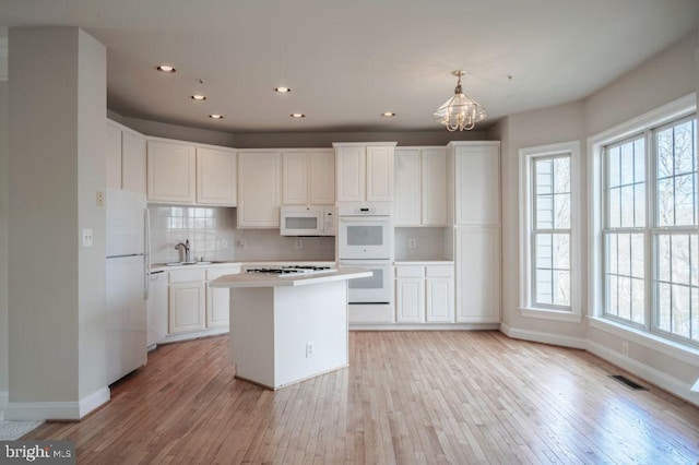 kitchen featuring pendant lighting, sink, white appliances, white cabinets, and a kitchen island