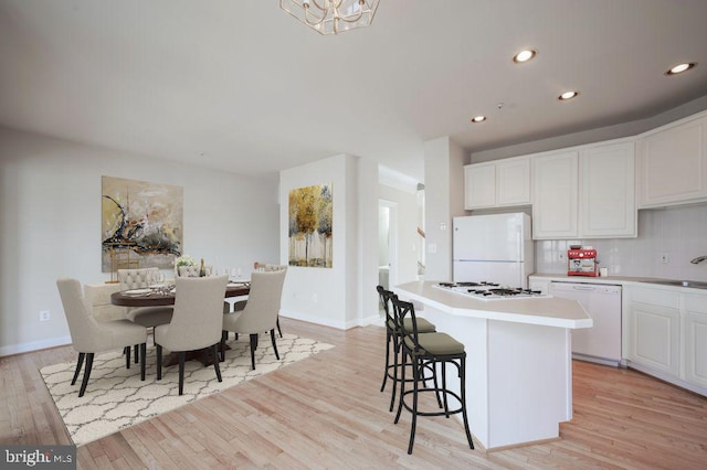 kitchen featuring white cabinetry, tasteful backsplash, a kitchen island, white appliances, and light hardwood / wood-style floors