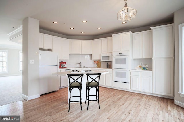 kitchen featuring light wood-type flooring, white cabinets, hanging light fixtures, a center island, and white appliances