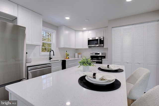 kitchen with tasteful backsplash, white cabinetry, appliances with stainless steel finishes, and light stone countertops