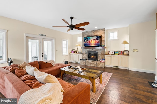 living room featuring a large fireplace, dark wood-type flooring, ceiling fan, and french doors