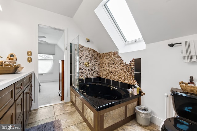 bathroom featuring vanity, vaulted ceiling with skylight, and a relaxing tiled tub