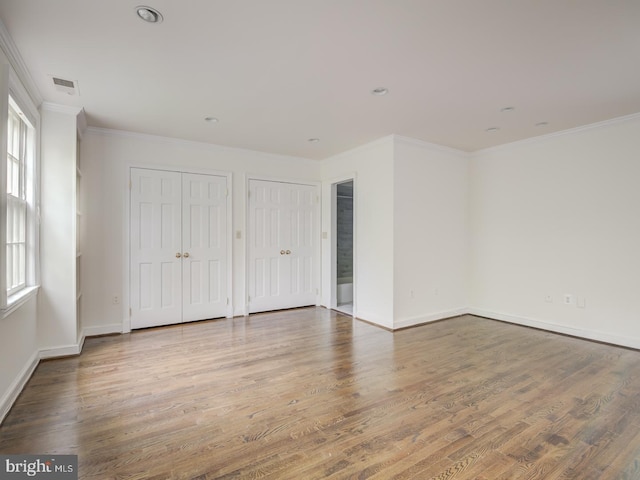 unfurnished bedroom featuring crown molding, wood-type flooring, and multiple closets