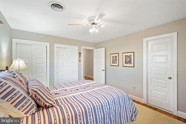 bedroom featuring hardwood / wood-style floors, two closets, and ceiling fan